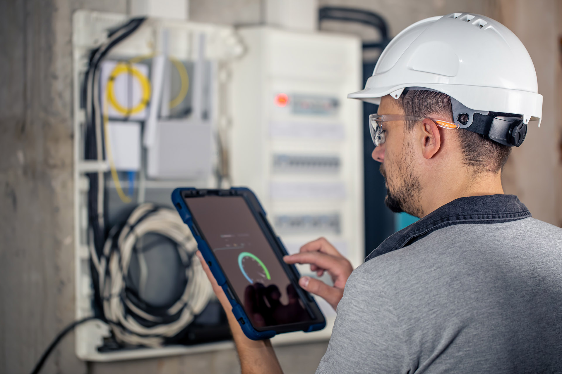 Man, an electrical technician working in a switchboard with fuses, uses a tablet.